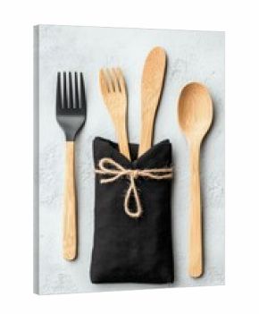 A flat lay of cutlery including a black fork, bamboo fork, bamboo knife, and bamboo spoon, arranged around a black cloth napkin tied with twine.