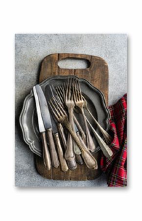 Overhead view of a stack of Vintage knives, forks and pewter plate on a wooden chopping board