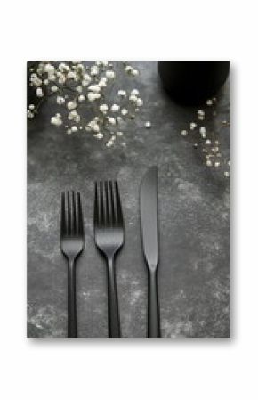 Elegant table setting with black cutlery and delicate white flowers on a dark background