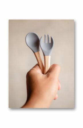 Fork and spoon, gray silicone baby eating utensils held in hand