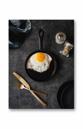 Top view fried egg in pan with plates cutlery on black background.