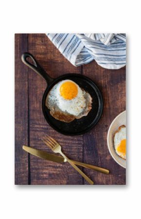 Top view fried egg in pan with plate cutlery on wood table.