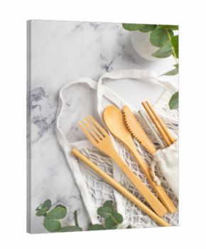 No plastic concept. Top view vertical photo of wooden cutlery fork spoon knife chopsticks white string bag steel straw cleaning brush and vase with eucalyptus on white marble background
