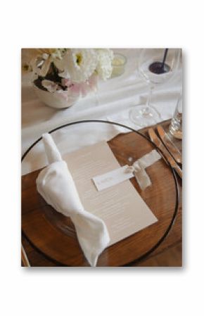 A beautifully set table with a clear glass plate, folded napkin, printed menu, and fresh floral arrangement, creating a refined and elegant atmosphere for a modern wedding table 