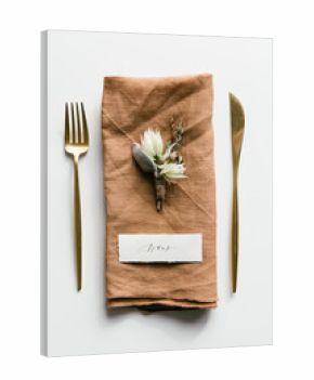 Table setting with golden colored cutlery styled with a orange linnen napkin, boutonniere and handwritten place card.