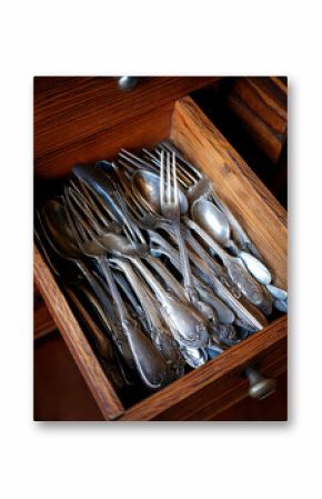 Closeup showcases tarnished silver cutlery nestled inside a rustic wooden drawer. Evokes vintage charm, memories, and home cooking. Ideal for food blogs or design projects.
