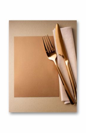 Gold cutlery on a napkin near a blank card. Shiny silverware set on a table. Preparing for a meal. Elegant place setting with a fork, knife, and empty paper. Restaurant concept.