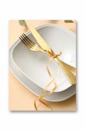 Elegant table setting with golden cutlery and ribbon on beige background, closeup