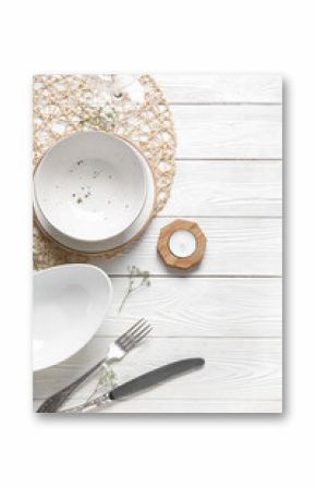 Wicker mat with plates, cutlery and candle on white wooden background
