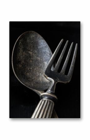 Ancient worn vintage cutlery on the black background. Crossed black metal spoon and fork in dark tone, Highlighting its texture and design, use it as your Space for text, Design, Wallpaper and Poster,