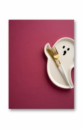Decorative vertical ghost-shaped plate with golden cutlery on a flat, vibrant magenta surface