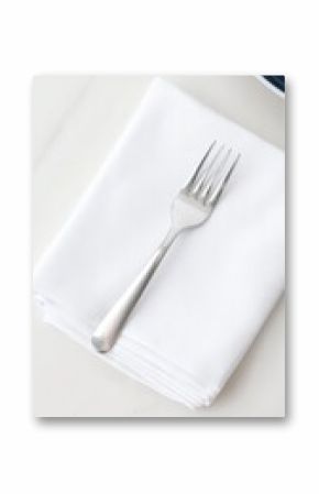 A pristine silver fork rests gracefully upon a crisp white linen napkin, embodying simple elegance and readiness for a refined dining experience.