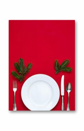 Festive Christmas table setting with red background and copy space for holiday greetings and seasonal celebrations featuring evergreen sprigs and elegant silverware