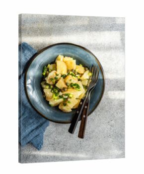 Overhead view of a bowl of traditional Greek potato salad (Patatosalata) on a table with cutlery and a napkin