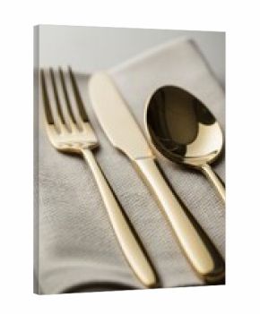 Polished gold cutlery set arranged neatly on a light beige linen napkin.