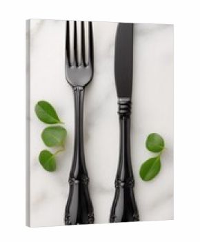 Black cutlery set on white marble with greenery