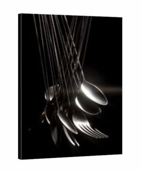 Dark conceptual still life of tumbling silver cutlery, suspended in air, harsh side lighting creating long shadows