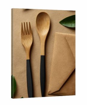 Eco friendly wooden cutlery with dark handles and green leaves arranged on a textured brown background