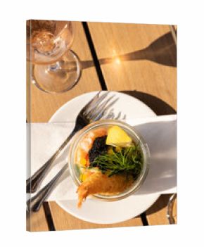 Shrimp salad with dill and lemon and a glass of rose on a wood table with silverware 