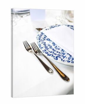 Empty, delft blue decorated ceramic dinner plate and silver cutlery arranged on a white table cloth. Top down view, no people