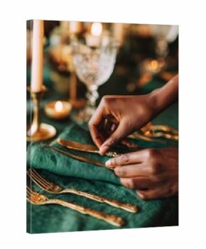 Hands arranging gold cutlery on a green table setting with warm candle light. Elegant festive dinner atmosphere. Concept: celebration, holiday, christmas, new year.