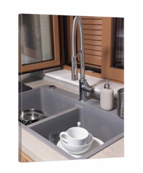 Horizontal close up of a stainless steel kitchen sink filled with dirty dishes, glasses, and cutlery on a stone counter. Focus on cleanup