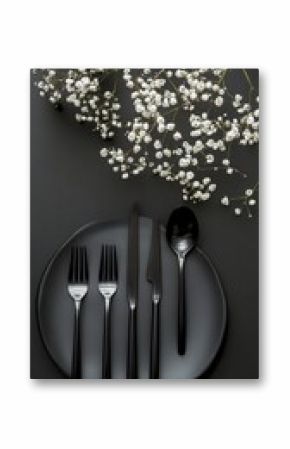 Elegant table setting with black cutlery and delicate white flowers on a dark background