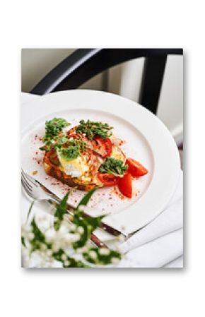 A colorful breakfast plate showcases poached eggs, sliced tomatoes, and fresh greens. The setting is inviting, with a subtle floral arrangement nearby, creating a warm ambiance