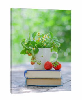 red strawberries and a cup with flowers on books on a table in the garden