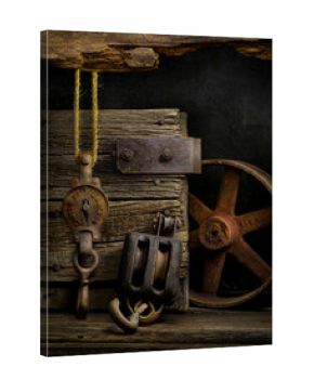 Old pulley, block and tackle, and iron wheel among old barn wood as still life art.