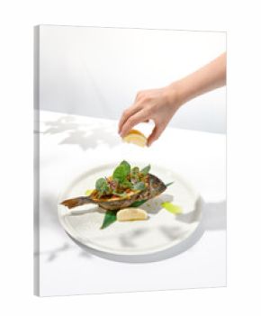 Roasted fish with female hand squeeze lemon. Person eat whole roasted fish with lemon juice. Action food menu. Female hand holding lemon over restaurant dish.