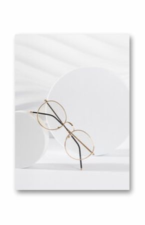 Unisex eyeglasses in a golden metallic frame on podium on white background. Vertical, close up. The product minimal still life. Optic store discount, sale. Copy space. Trendy eyewear photography