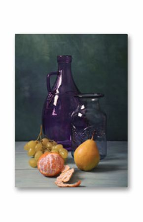 Still life with blue glass vase, lilac glass jar and fruit on turquoise background