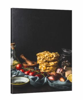Homemade italian pasta with cooking ingredients on dark rustic kitchen table at wall background. Copy space. Italian cuisine. Still life