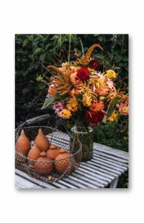 Freshly harvested garden bouquet in autumn colors on rustic bench with handmade clay vessels. This image reflects slow floristry, seasonal abundance, sustainable living, craft heritage