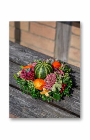 Decorative autumn wreath featuring a striped green gourd and colorful natural elements on a wooden bench.