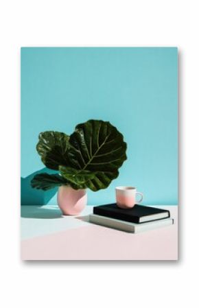 Stylish plant, cup, and notebooks on a pastel background