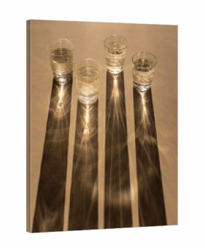 Four glasses of sparkling water casting long shadows on a beige background, light and shadows art