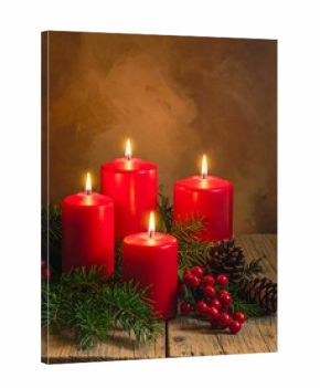 Four burning red candles, greenery, and pinecones on a wood surface