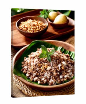 A wooden bowl of seasoned minced meat and rice on a banana leaf, garnished with fresh mint, top view.