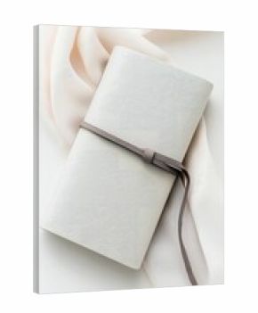 A close-up, top-down shot of a wrapped notebook with a ribbon, resting on a soft fabric. The scene is bathed in soft, natural lighting, creating a minimalist an