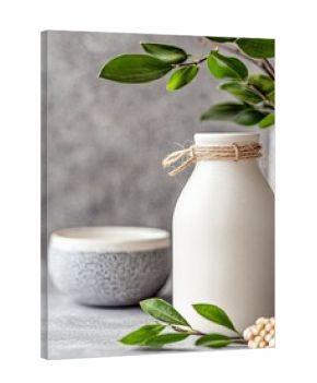 A white bottle with twine tied around the neck, a gray bowl, and green leaves are arranged on a gray background. The scene is lit with soft, natural light.