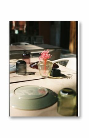 Pink flowers in a glass vase on a sunlit cafe table