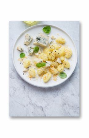 Plate of italian potato gnocchi served with blue cheese, vertical shot on a white stone background with space, elevated view