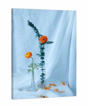 Verticl shot of cute orange still life flowers placed in a glass vase with white sheets behind them