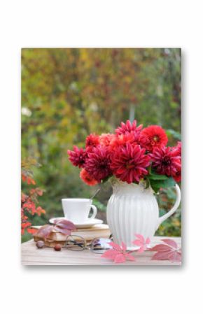 Vase with red autumn flowers and books on the table in the autumn garden. Autumn still life