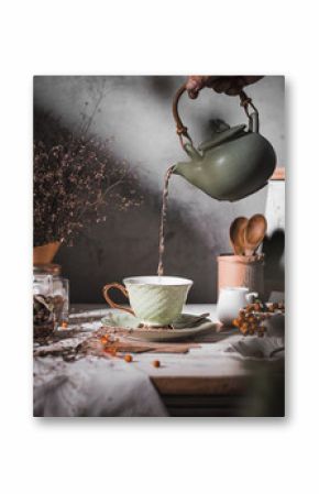 Pouring tea in to green ceramics cup on the table. Selective focus, conceptual stilllife darkmood photography