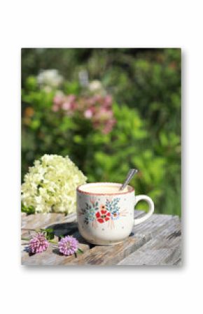 A beautiful ceramic coffee cup  with flowers on the wooden table in the garden. Selective focus. 