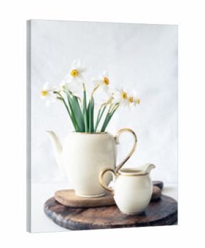 Still life with a blooming bouquet of white daffodils in an elegant porcelain teapot on a textured white background