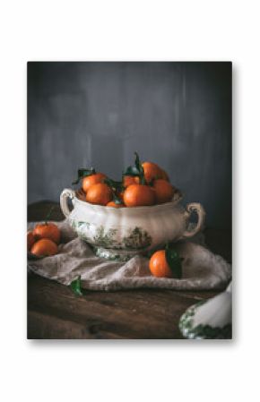 Sophisticated still life with ripe orange tangerines with green leaves in deep white bowl on table on gray background